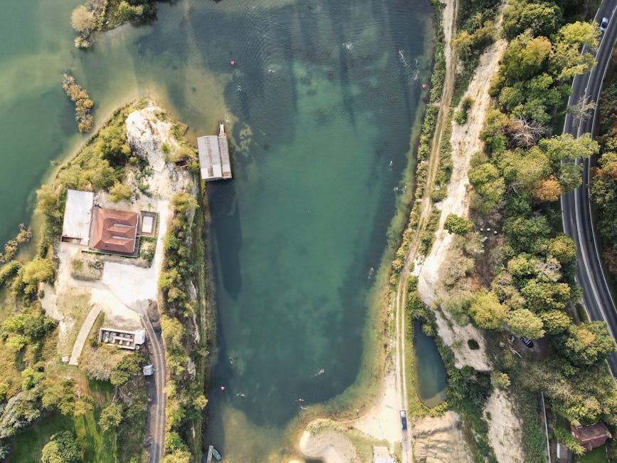 An aerial view of a circular artificial lake surrounded by wooded hills during late afternoon or early evening, with the sun casting a warm glow on the water and trees. The lake's shoreline features a